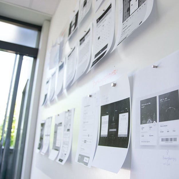 Printed resumes and documents pinned on a whiteboard in an office.
